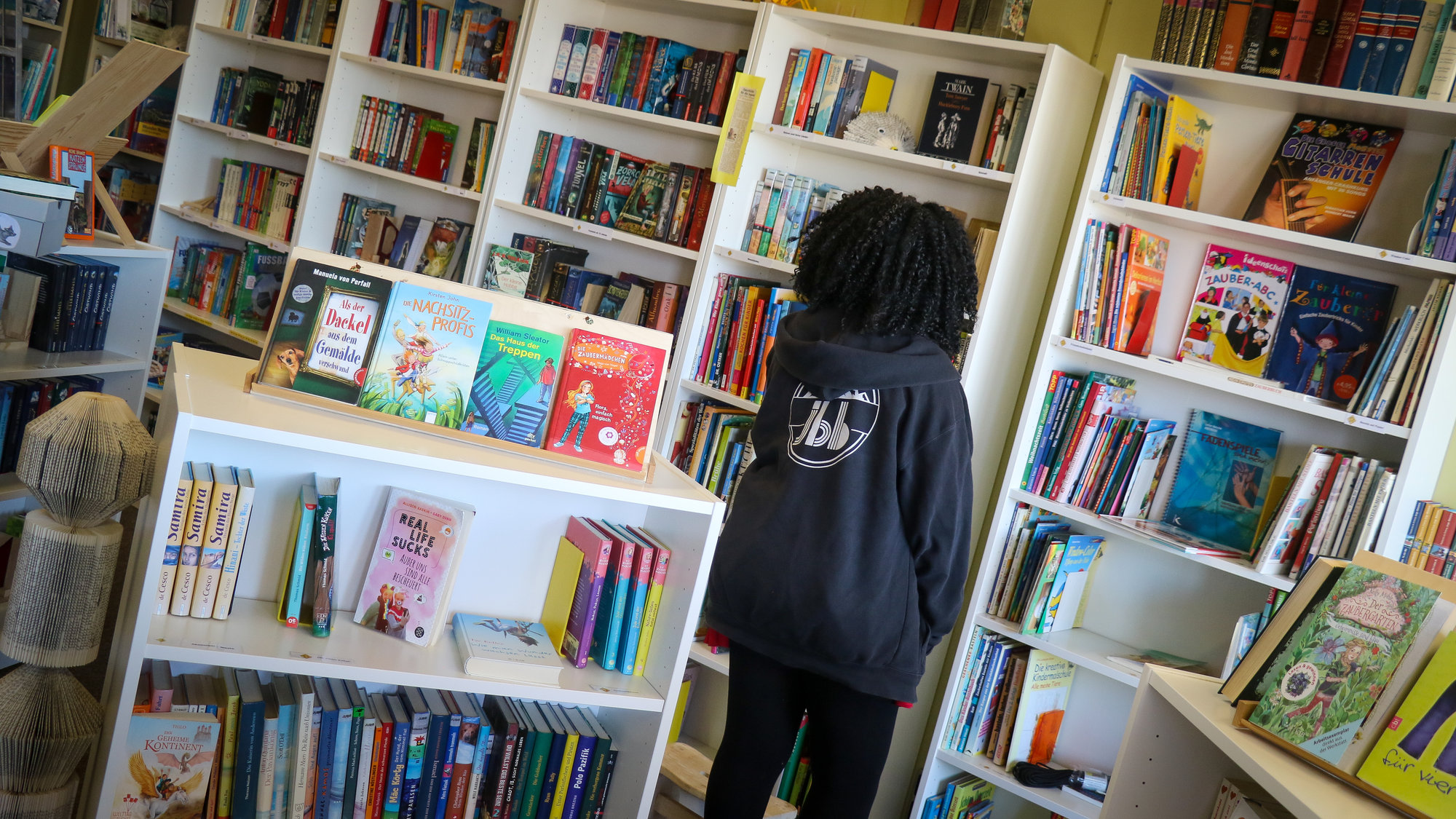 Schülerin steht vor Bücherregal und sucht sich ein Buch aus. | © Thomas Metschl